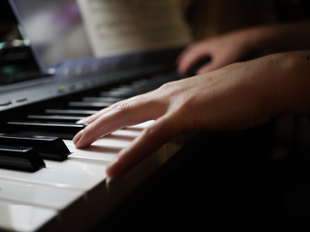 hands playing a digital keyboard with sheet music
